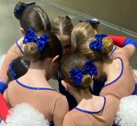 A group of girls with blue bows in their hair are huddled together
