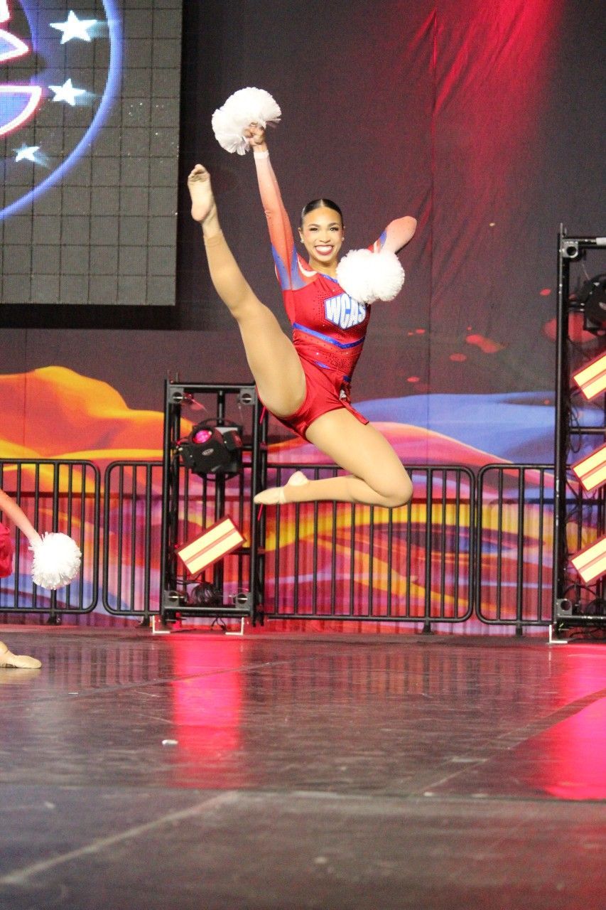 A cheerleader is jumping in the air while holding a pom pom