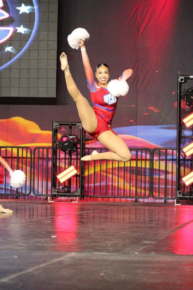A cheerleader is jumping in the air while holding a pom pom