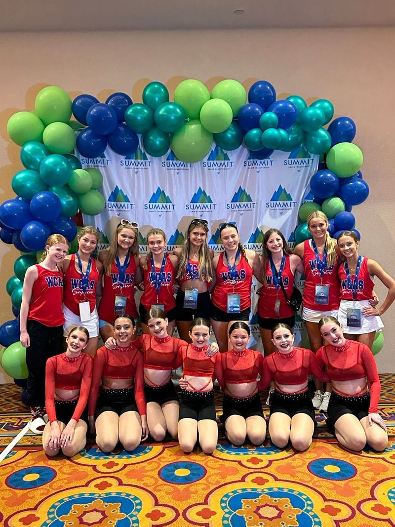 A group of young girls are posing for a picture in front of balloons.
