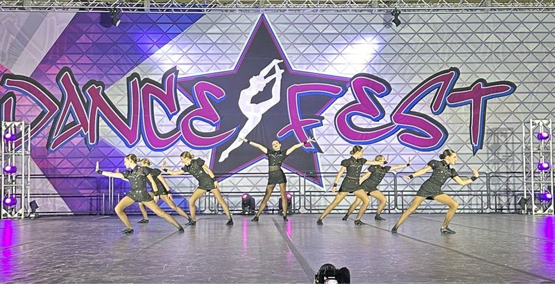 A group of dancers are performing on a stage in front of a dance fest sign.