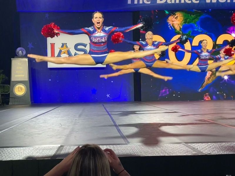 A group of cheerleaders are performing on a stage in front of a sign that says ias