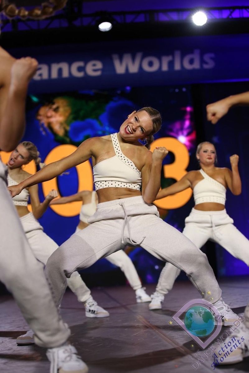 A group of women are dancing in front of a sign that says dance worlds