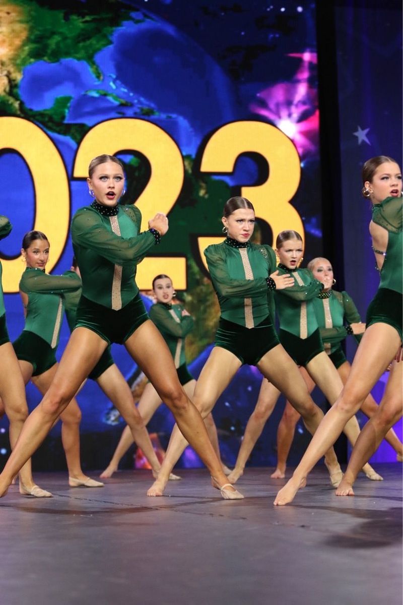 A group of dancers are performing on a stage with the number 023 in the background.