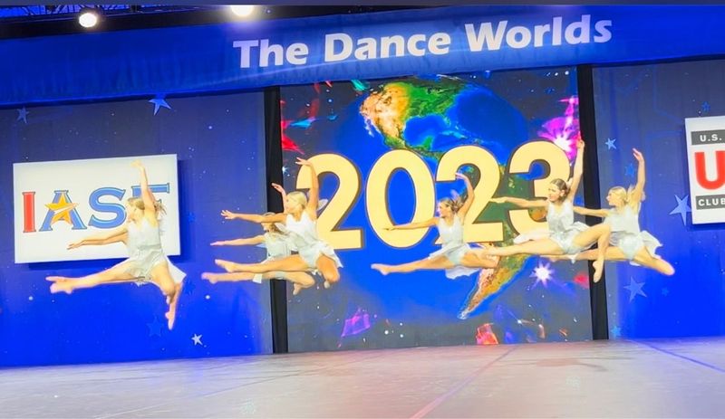 A group of dancers are performing in front of a sign that says the dance worlds