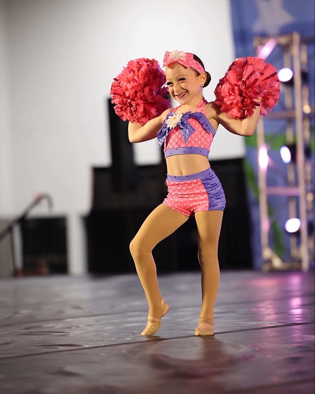 A little girl in a cheerleader outfit is holding pink pom poms