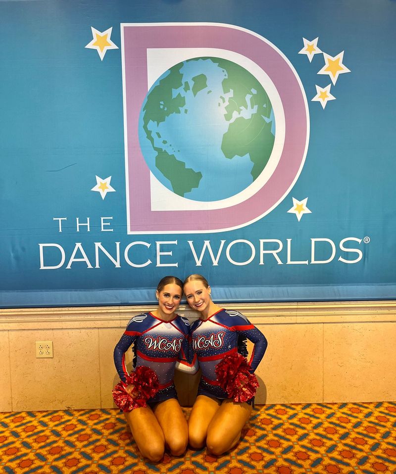 Two cheerleaders pose in front of a dance worlds sign