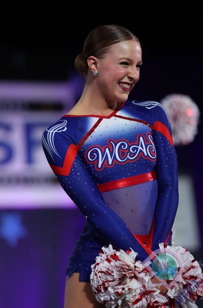 A cheerleader in a blue and red uniform is smiling and holding pom poms.