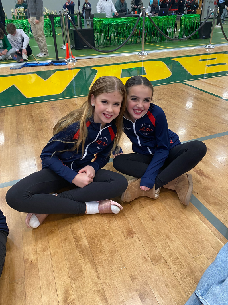 Two young girls are sitting on the floor of a gym.