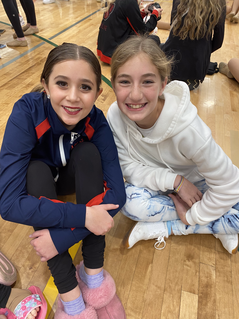 Two young girls are sitting on the floor in a gym.