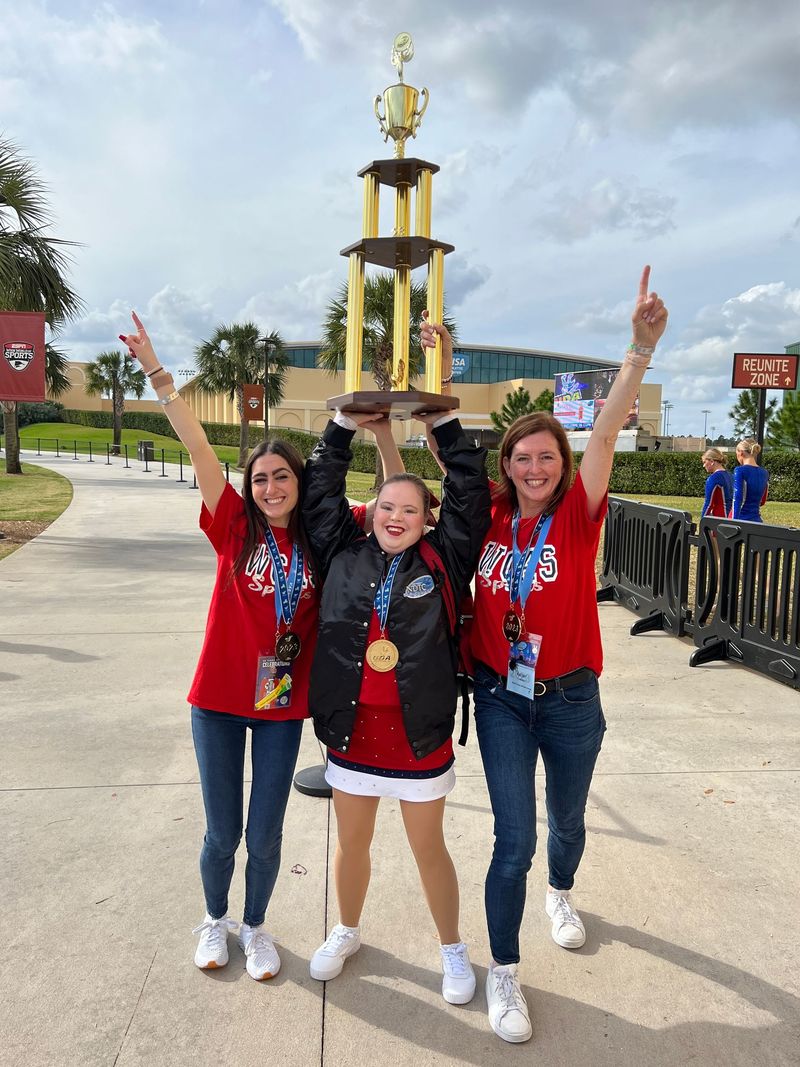 Three women are standing next to each other holding a trophy over their heads.