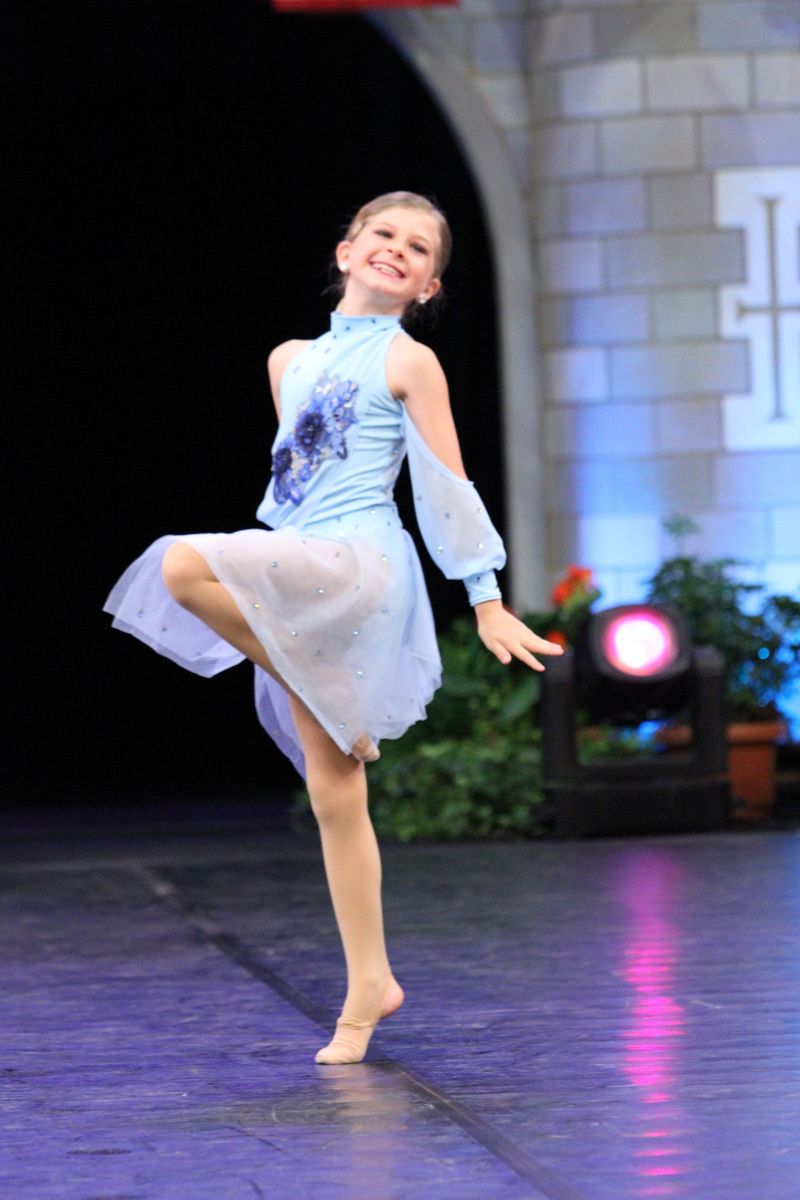 A young girl in a blue and white dress is dancing on a stage.