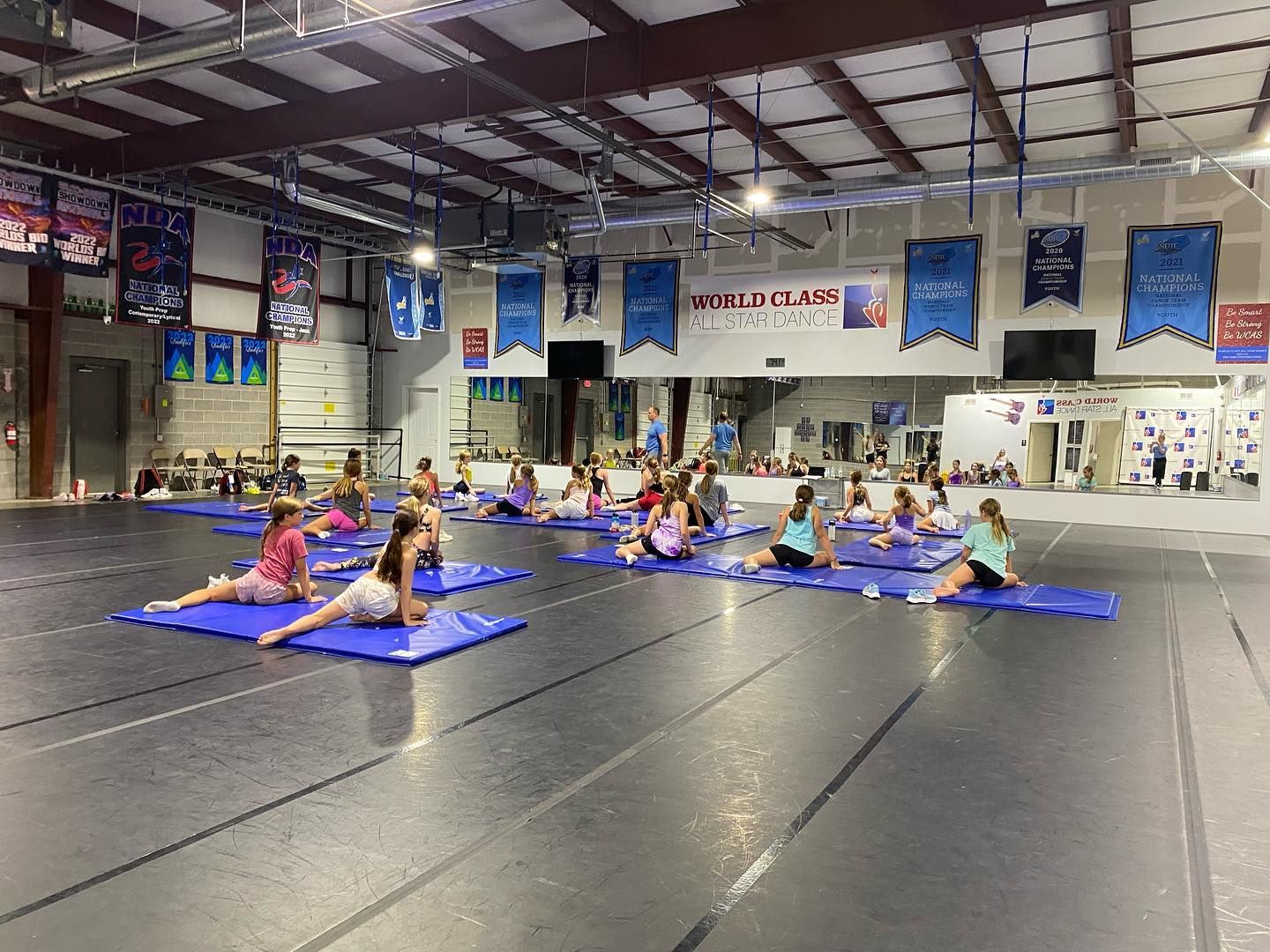 A group of children are sitting on yoga mats in a dance studio.