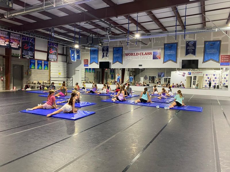 A group of children are sitting on yoga mats in a dance studio.
