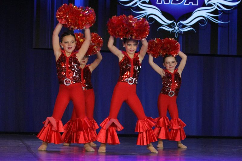 A group of young girls in red outfits are holding up red pom poms