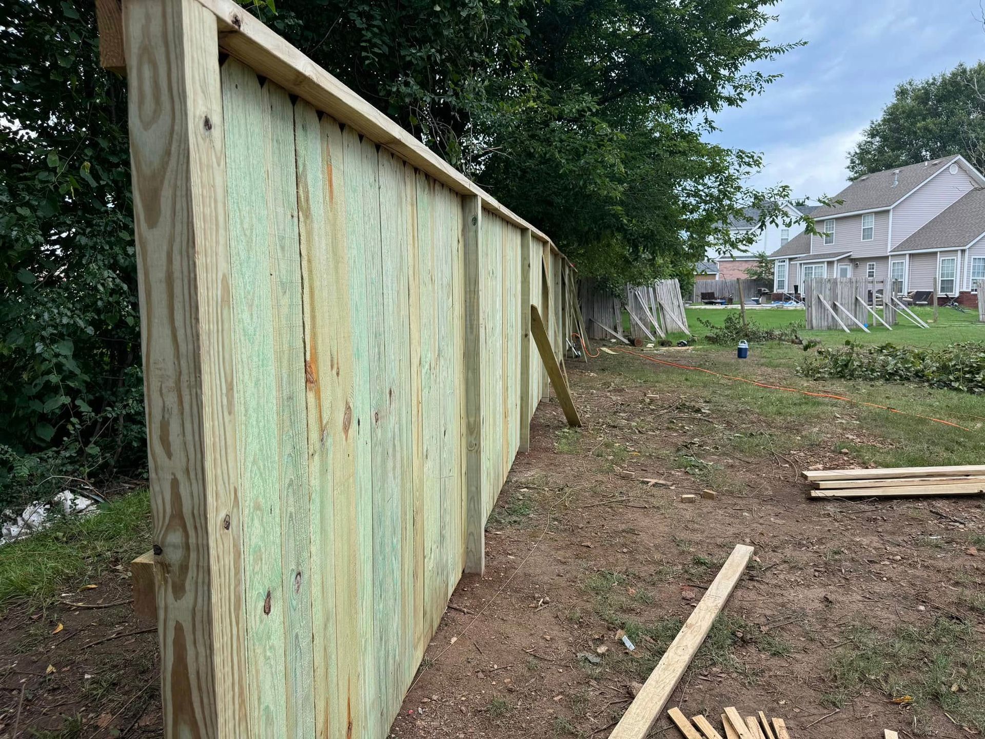 Wooden fence being constructed in a yard, green-toned wood, cloudy sky background.