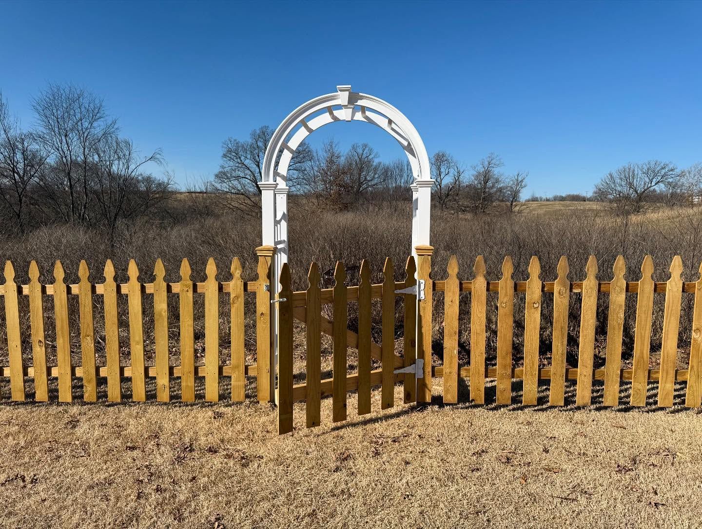 Woman in straw hat smiles, holding wine glass near a lake.