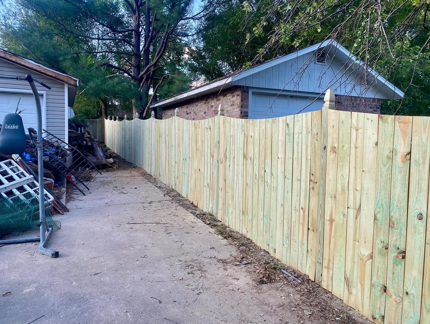 Wooden fence runs along a gravel driveway, beside a small white building and a brick garage.