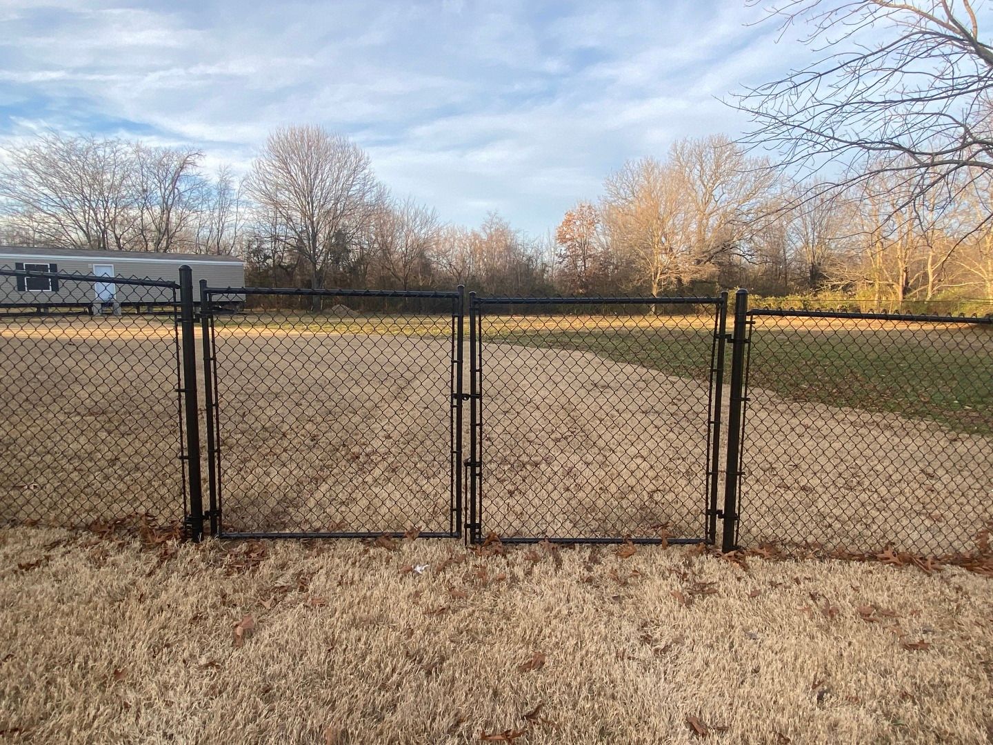 Black chain-link fence with double gate in a yard. Trees and blue sky background.