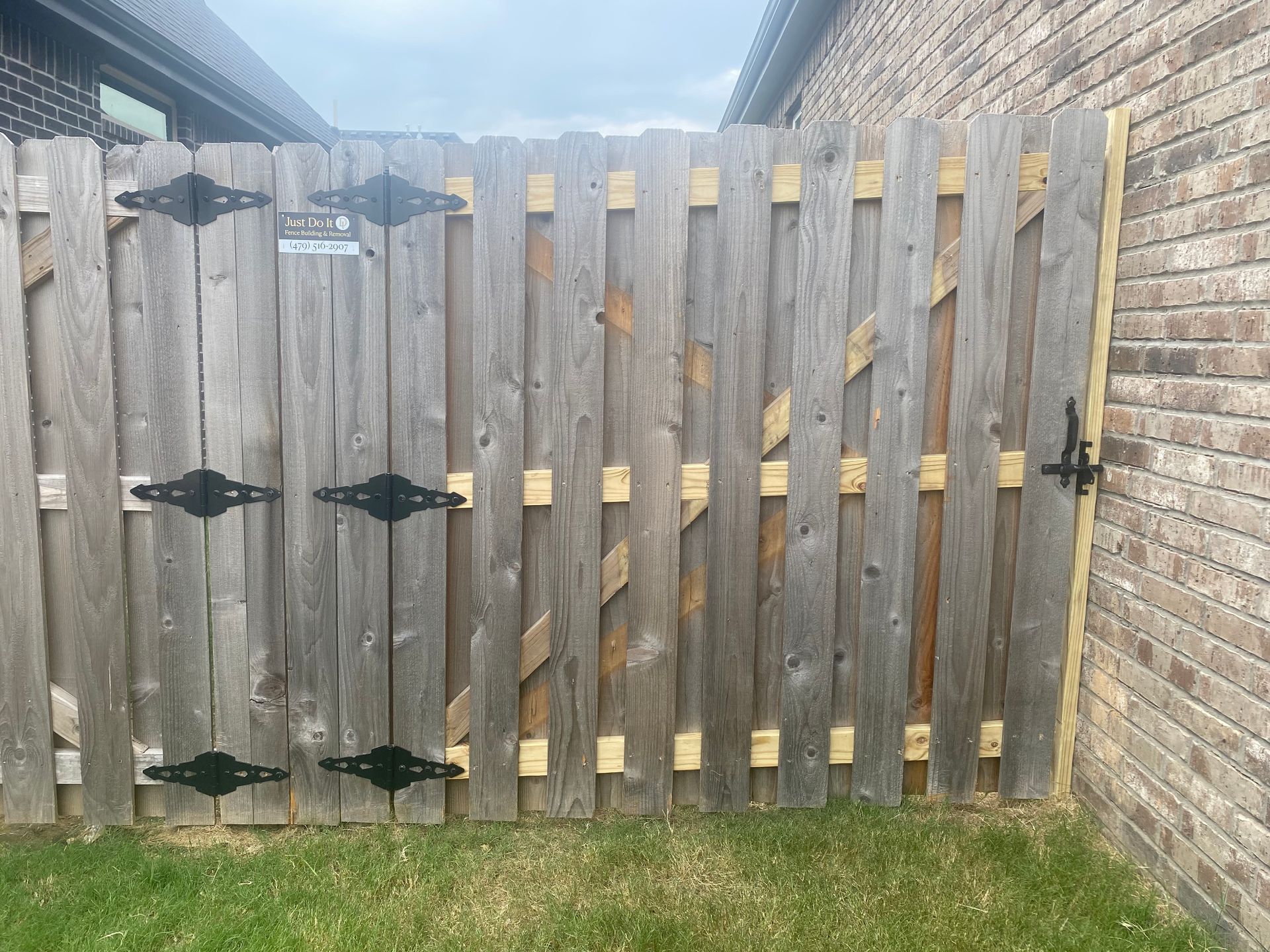 Wooden gate in a backyard, attached to a brick wall. The gate has black hinges and latch.