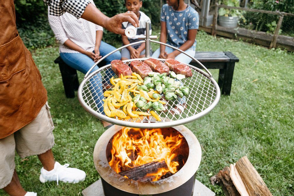 A patio features a bright green outdoor sofa, a dark wooden side table with potted plants, and a white, shingled wall.