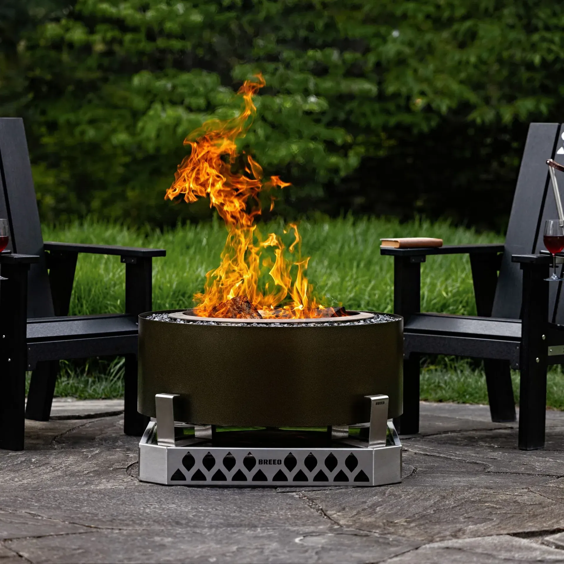 Burning fire pit with tall flames between two black chairs on a patio