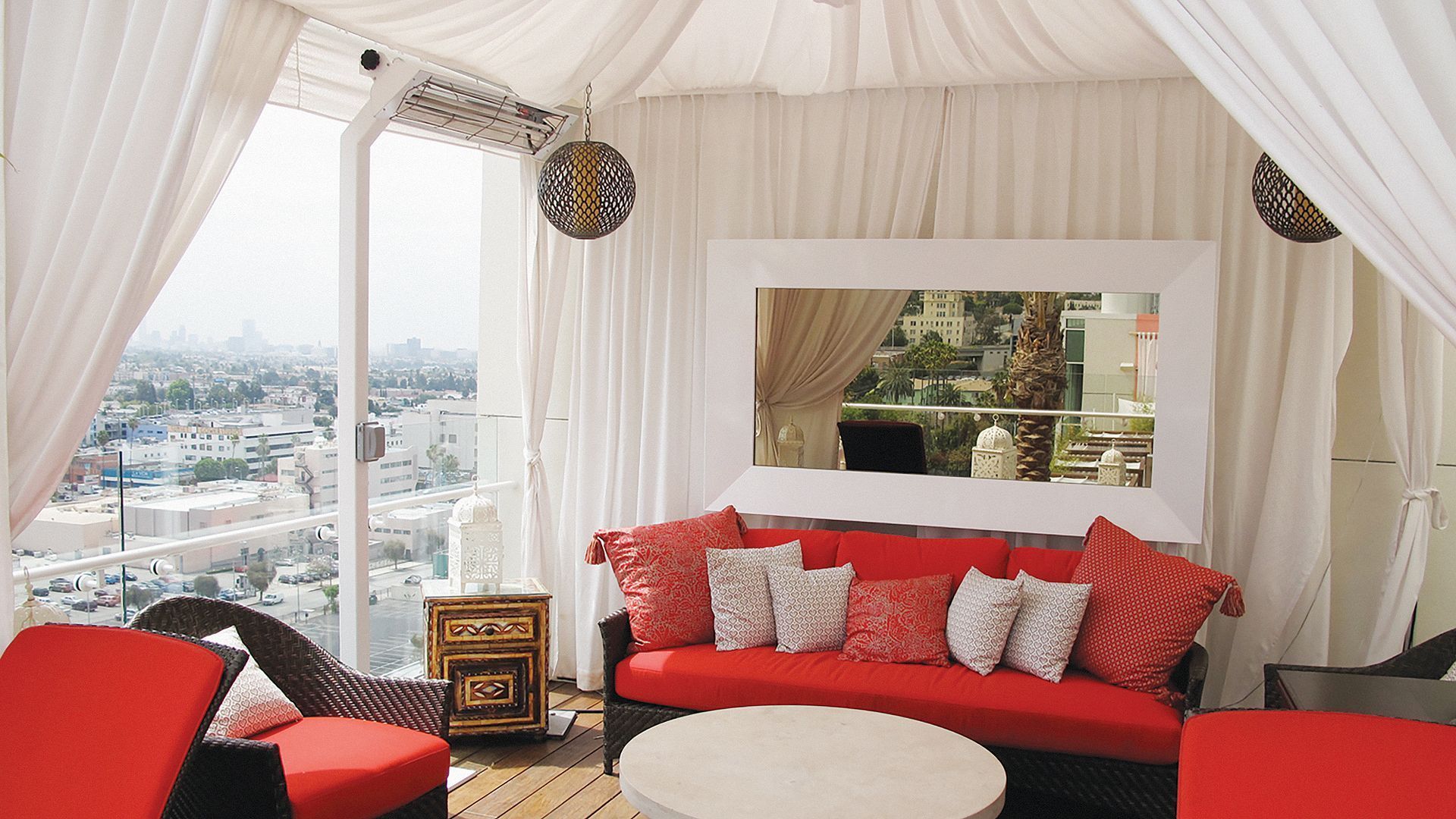 A smiling person with dark hair, wearing a red cable-knit sweater against a neutral, paneled wall background.