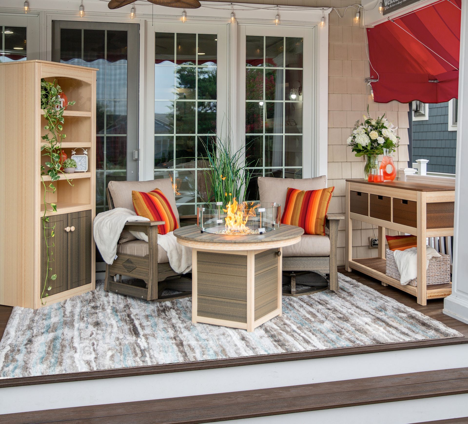 Cozy outdoor patio with a fire pit, two armchairs, a shelving unit, and a console table on a patterned rug.