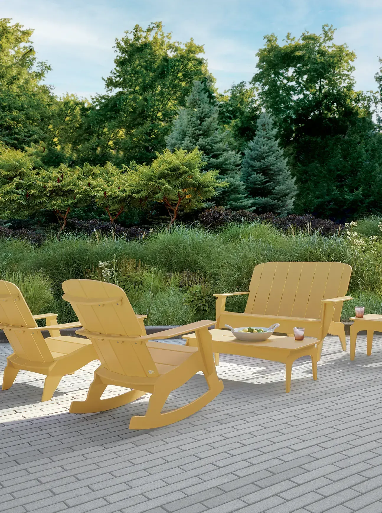 A patio features a bright green outdoor sofa, a dark wooden side table with potted plants, and a white, shingled wall.