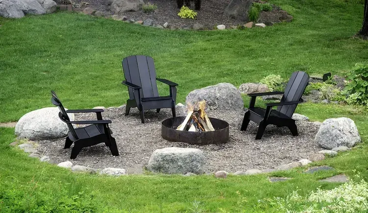 Two light-colored Adirondack chairs with a shared table sit on a lush lawn near a metal armillary sphere garden ornament.