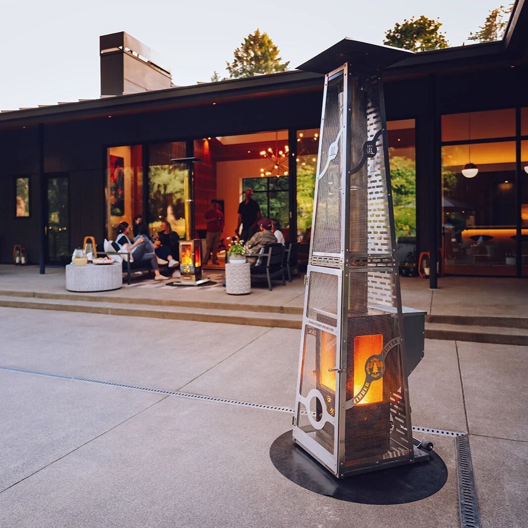 A patio features a bright green outdoor sofa, a dark wooden side table with potted plants, and a white, shingled wall.
