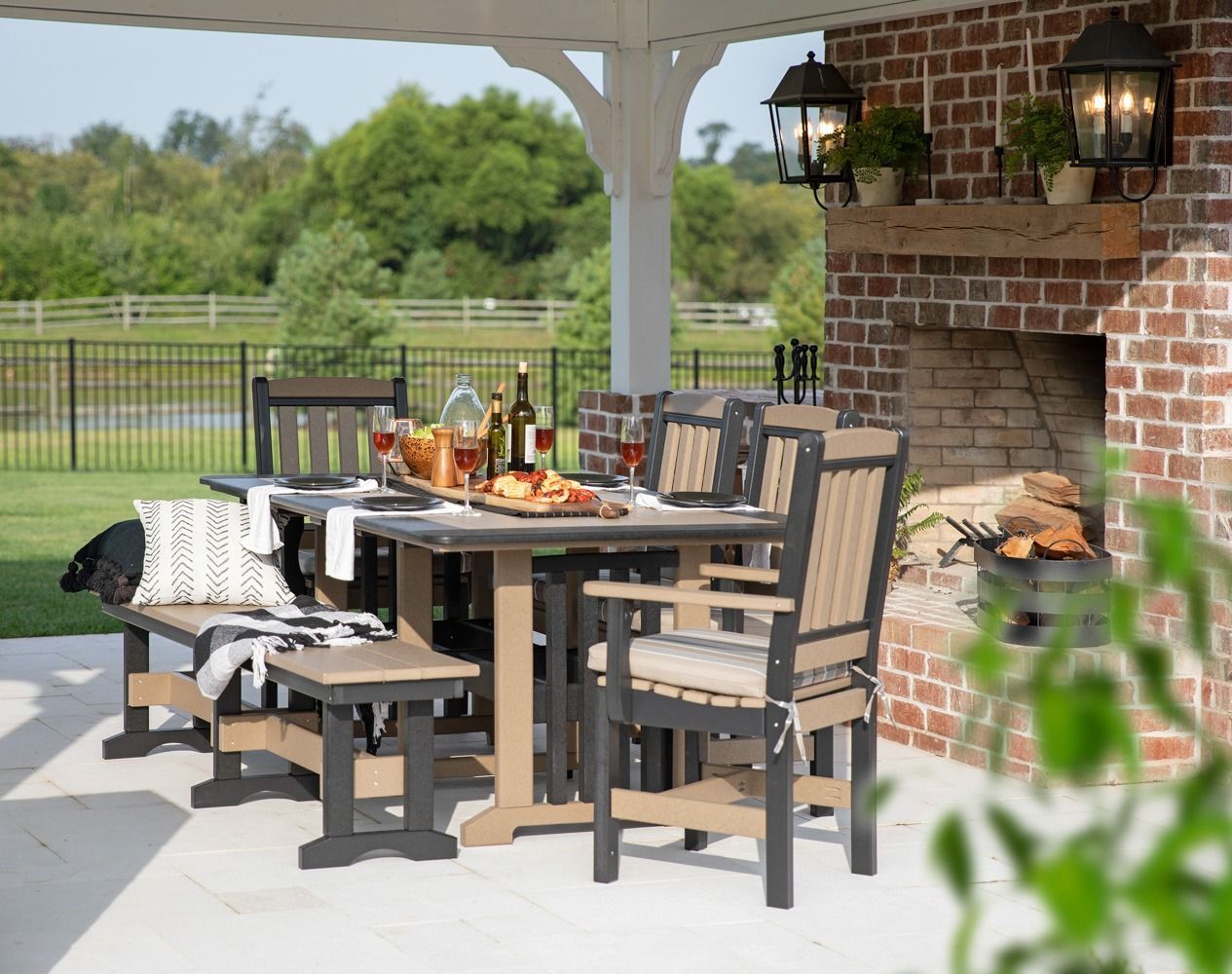 A light wood dining table set for four with woven placemats, dark plates, and a glass-enclosed tabletop fire pit.