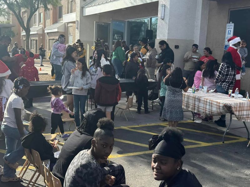People at an outdoor event with tables and a building; a Santa Claus is present, festive.