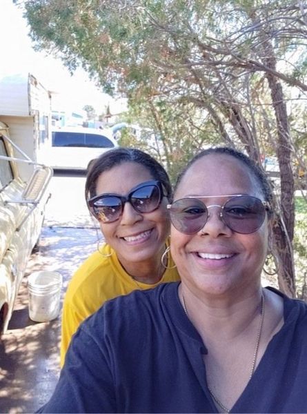 Two women in sunglasses smiling outdoors, near a vehicle.