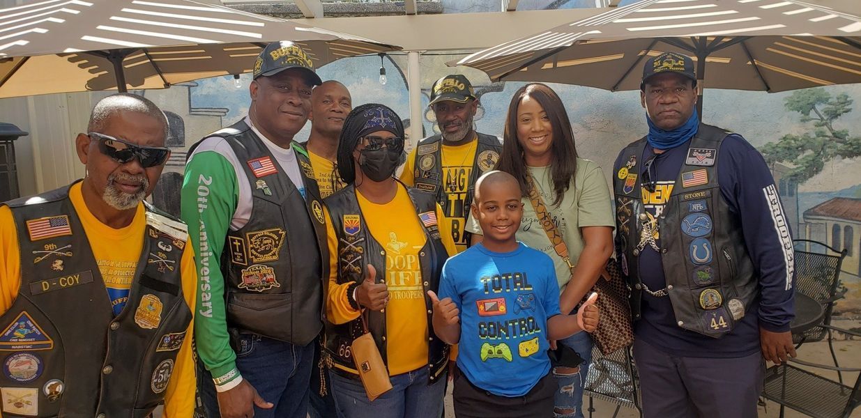 Group of people in vests, hats, and yellow shirts posing outdoors with a boy in a blue shirt.