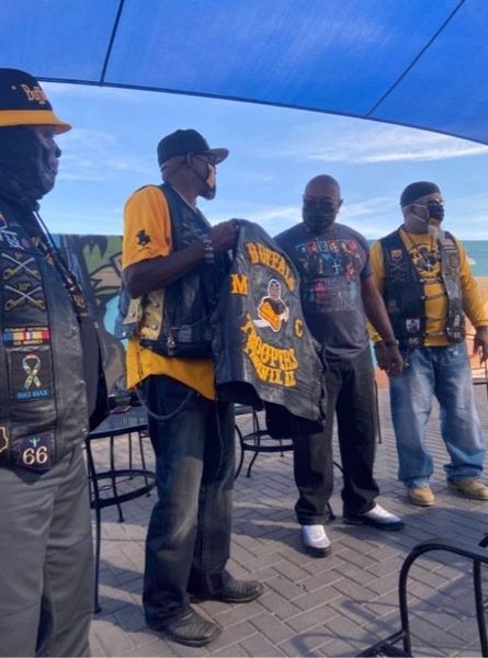 Men in biker vests stand outside; one holds a vest with 