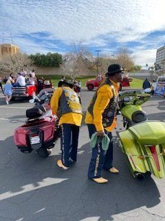 Two people wearing matching outfits stand near customized motorcycles in a parking lot.