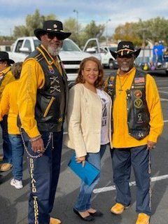 Two men in yellow shirts and vests, one woman in a cream blazer posing outdoors.