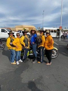 Group of people in cowboy hats and riding gear posing with a motorcycle in a parking lot.