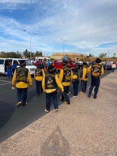 Group of people in yellow vests and black patches walk toward parked vehicles in a lot.