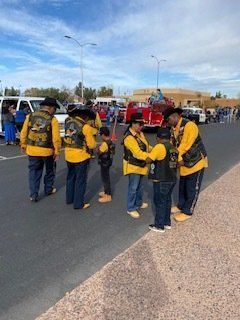 Group of people in yellow vests and jackets on a street, possibly a parade or event, with a fire truck in the background.