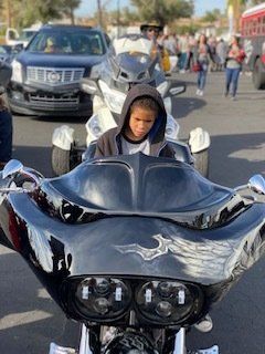 Child in a hooded sweatshirt sits on a motorcycle, with a trike motorcycle in the background.
