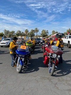 Motorcycle riders in yellow vests lined up on a sunny day.