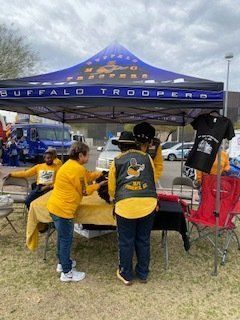 People at a Buffalo Troopers booth, selling merchandise. Yellow shirts, blue tent, and outdoor setting.