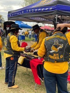 People at a Buffalo Troopers booth, selling merchandise. They wear yellow shirts, vests, and hats.