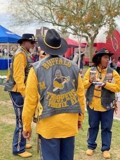 Three people wearing yellow shirts, blue pants, and vests that say 