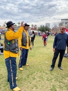 Three men in a park. Two wear yellow shirts, vests, and blue pants with 