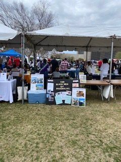 Outdoor event with tents and tables. Sign reads “Black Men of Phoenix, AZ”. People stand near booths.