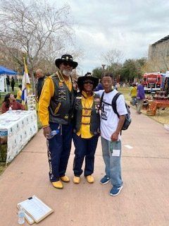 Three people in yellow and black vests, standing outside.  A man and woman are wearing cowboy hats. The younger person is wearing a backpack.