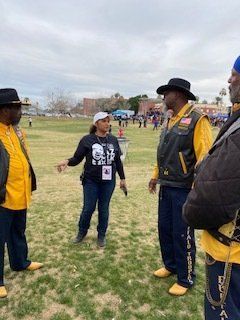 Woman speaks to three men in biker vests outdoors on grass.